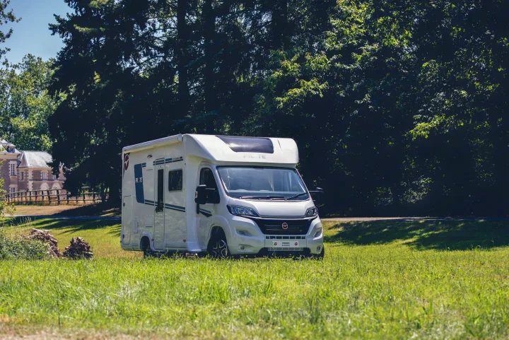 White campervan for rv rental parked on green grass in a sunny countryside setting, with trees and a building in the background.. Pilote P696D ESSENTIEL 2024