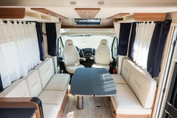 Bright RV interior featuring a clean dinette with white leatherette seating and a gray table, plus the cockpit. Perfect for your next rv rental.. Pilote P696D ESSENTIEL 2024