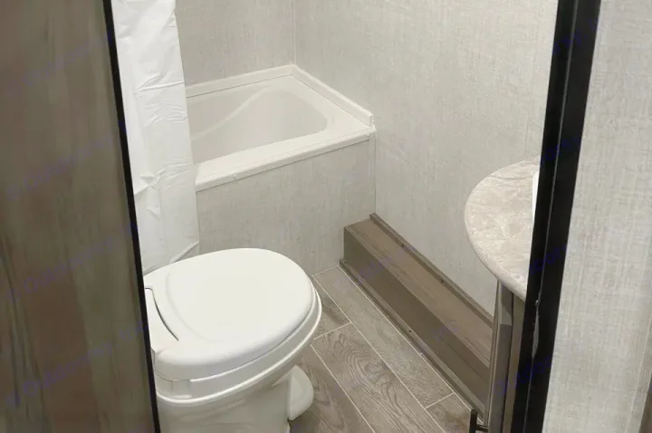 Discover a compact RV rental bathroom with a white toilet, small tub/shower, and half-round sink, showcasing efficient design.. Grand River 22MB 2024