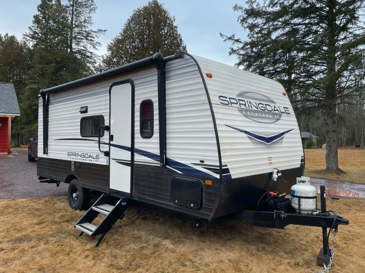 This Springdale Keystone travel trailer is available for your next RV rental adventure, parked on dry grass near trees.. Keystone RV Springdale 2023