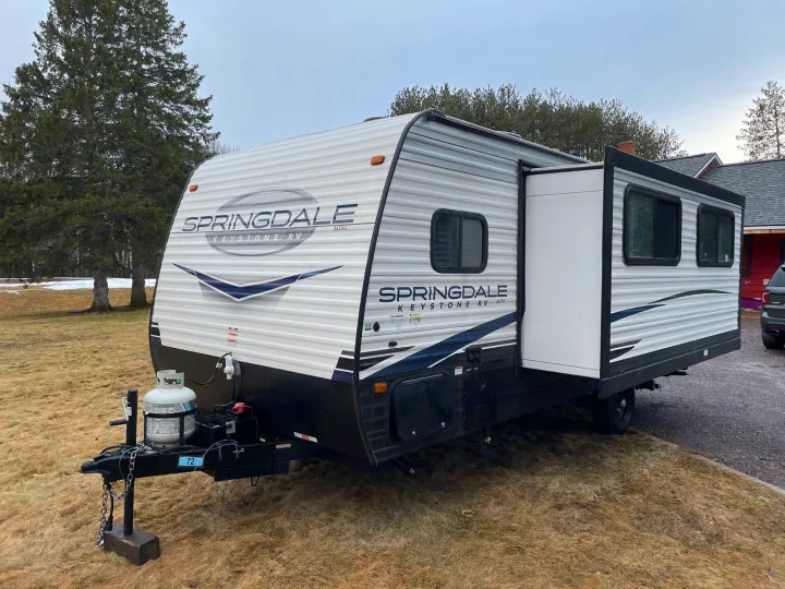 White Springdale Keystone RV travel trailer with an open slide-out, ideal for an RV rental and outdoor adventures.. Keystone RV Springdale 2023