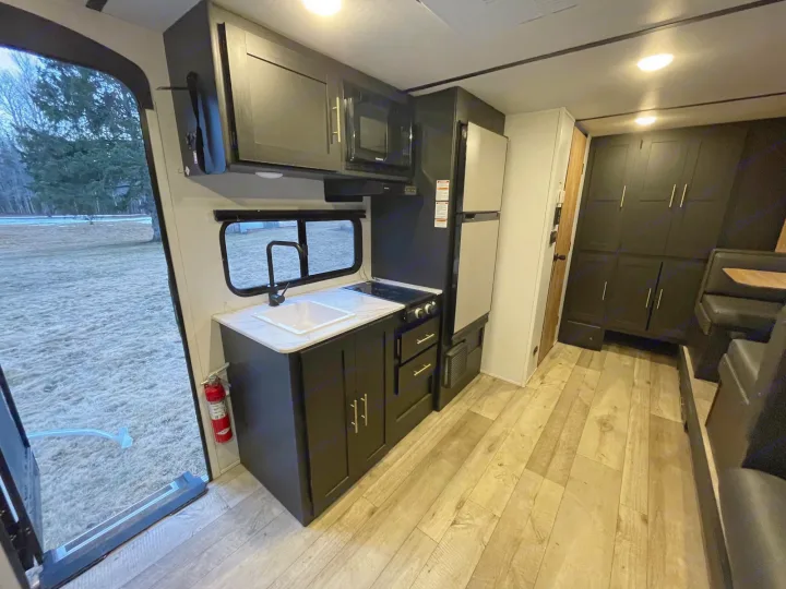 RV rental interior: a modern kitchen with black cabinets, appliances, and light wood-look flooring.. Keystone RV Springdale 2023