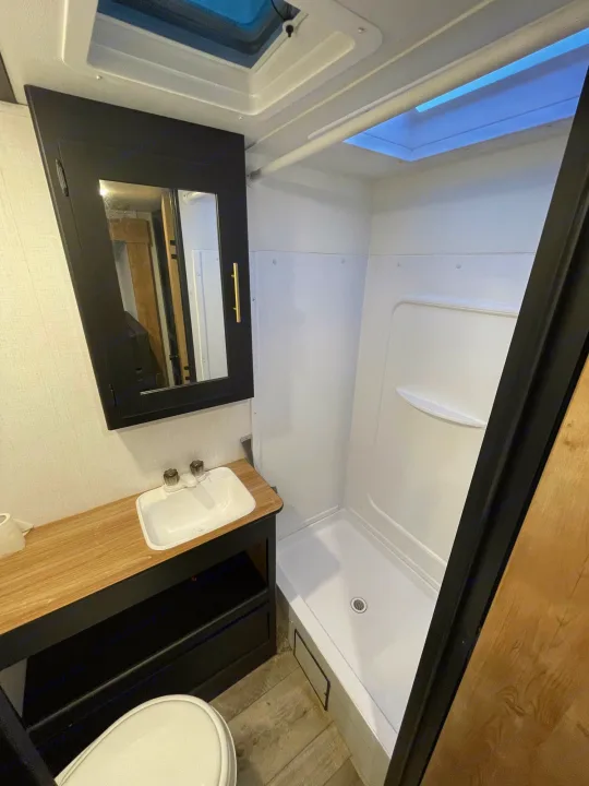 Modern RV rental bathroom with sink, toilet, shower, and ceiling skylight. Bright and functional space.. Keystone RV Springdale 2023