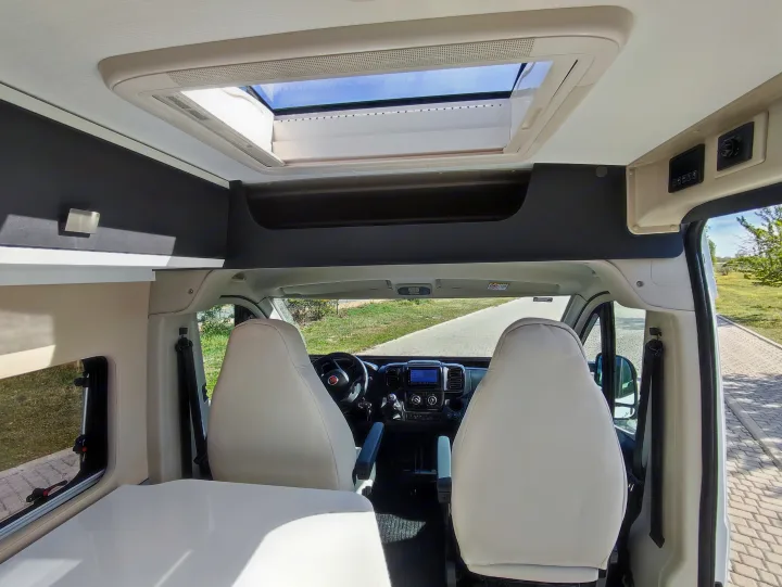 Spacious RV rental interior with front cockpit view, comfortable seating, and an open skylight, ideal for travel.. McLouis Menfys Van 3 Maxi 2024