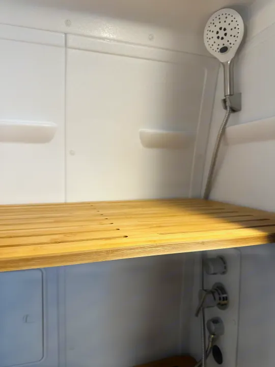 Modern RV rental shower interior features a slatted wood bench, white walls, and a handheld shower.. Mercedes-Benz Entegra Launch 2024