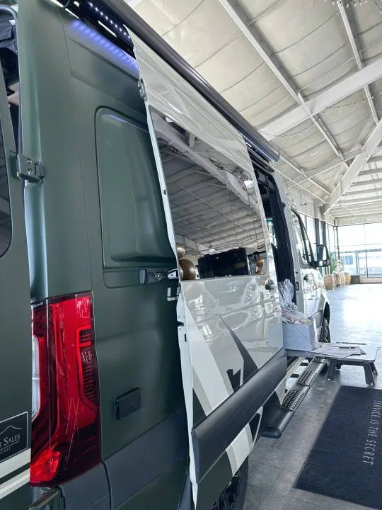 Custom dark green RV rental van with side door open, revealing interior features and an exterior setup under a white ceiling.. Mercedes-Benz Entegra Launch 2024