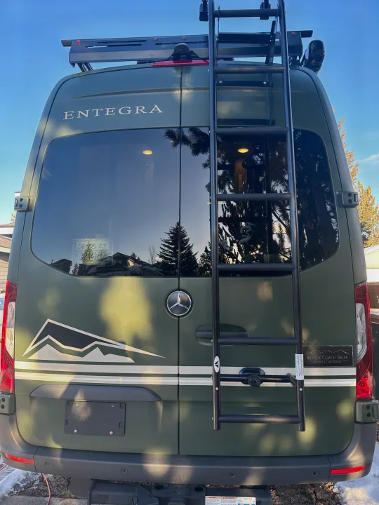 Rear of an olive green Mercedes-Benz Sprinter camper van, equipped with a roof rack and ladder, perfect for RV rental exploration.. Mercedes-Benz Entegra Launch 2024