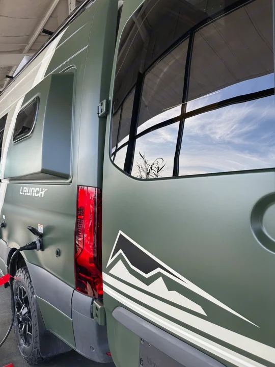This green "LAUNCH" camper van is hooked up, ready for your next RV rental adventure. A mountain graphic adorns the side.. Mercedes-Benz Entegra Launch 2024