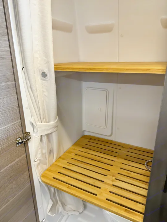 RV rental shower: compact design with white curtain, magnetic closures, bamboo shelves, and a slatted floor mat for utility.. Mercedes-Benz Entegra Launch 2024