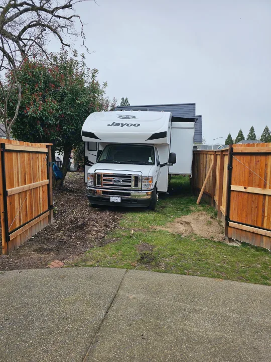 A white Jayco rv rental motorhome is parked in a fenced residential yard. Its slide-out is extended, ready for use.. Jayco Redhawk 2023
