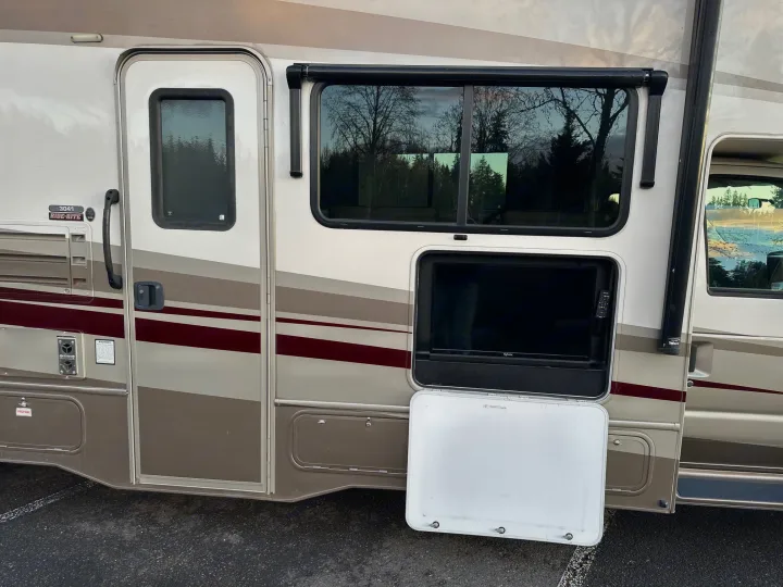 Side view of an RV rental. Features include an open exterior TV compartment, entrance door, and windows.. Forester Forester Motorhome 2020