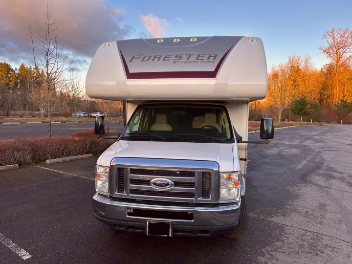 Front view of a white Class C Forester RV rental, parked in a lot with trees under a blue sky. Ready for your next adventure!. Forester Forester Motorhome 2020