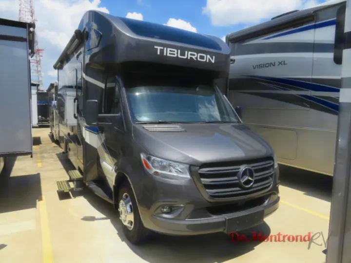 Dark grey Mercedes-Benz Tiburon Class C RV rental, with deployed steps, parked on a sunny lot amidst other RVs.. Thor Tiburon 2023