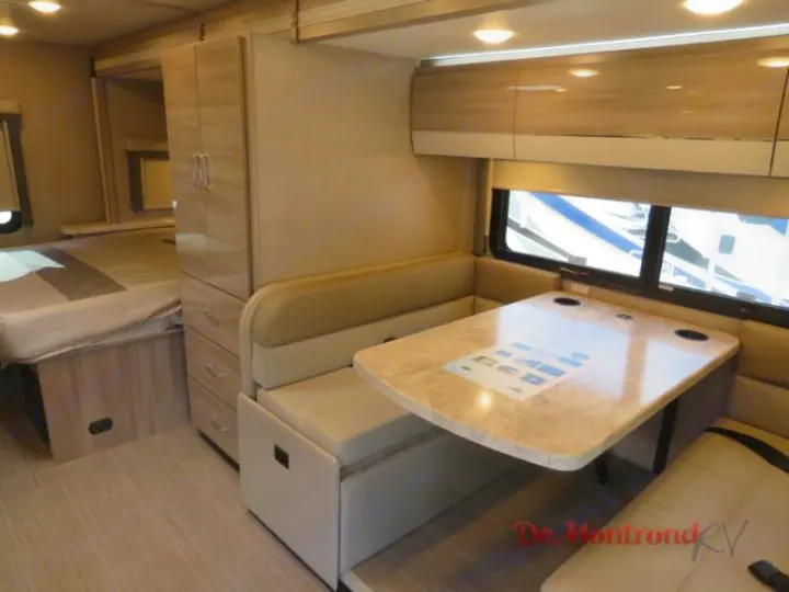 This RV rental interior features an L-shaped dinette with a table, window, nearby bed, and storage cabinetry.. Thor Tiburon 2023