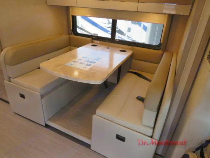 Inside an rv rental: a cozy beige dinette with U-shaped seating, a light marble-patterned table, and a window view.. Thor Tiburon 2023