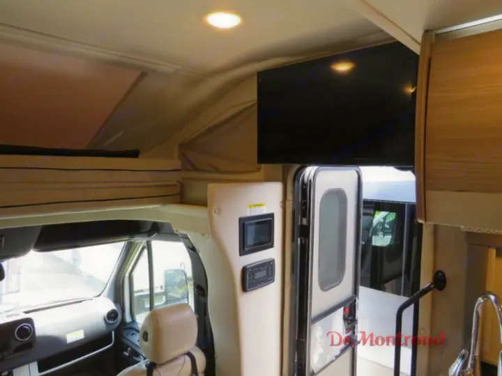 RV rental interior: overhead bunk, flat-screen TV, control panel, and entry door, with driver's cab visible.. Thor Tiburon 2023