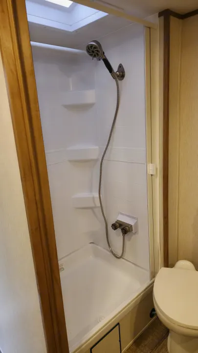 Inside an RV rental: a bright, white shower stall with a skylight, handheld shower, and a toilet to the side.. Forest River 22sw-l 2024