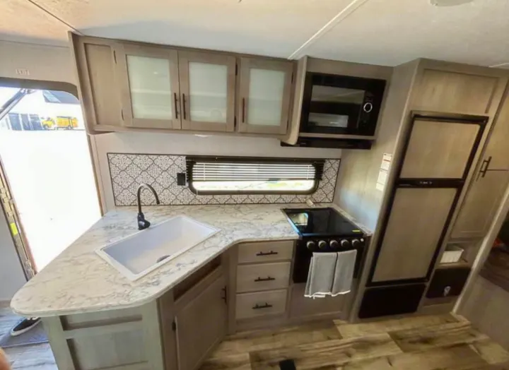 RV rental kitchen interior: light wood-look cabinets, marble-look counter, sink, stove, microwave, fridge, and backsplash.. Coleman Lantern lt 2023