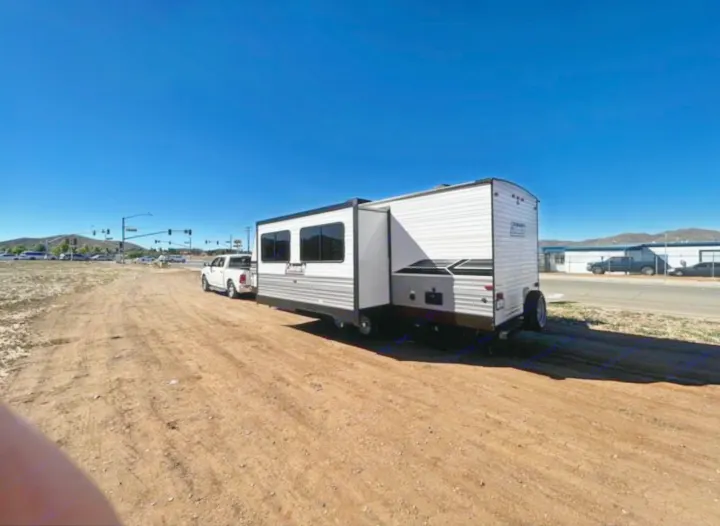 Outdoor RV rental: White truck towing a travel trailer with extended slide-out on a dirt lot.. Coleman Lantern lt 2023
