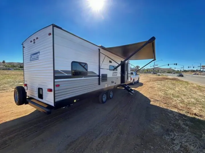 Sunny Coleman travel trailer RV rental parked on dirt, awning extended, with truck. Ready for your next adventure!. Coleman Lantern lt 2023