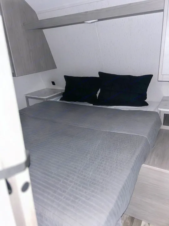 RV rental interior: A neat bedroom with a gray bed, black pillows, and compact side tables on either side.. Coleman Lantern lt 2023