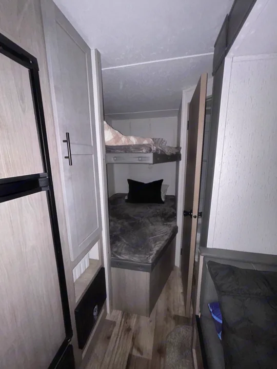 Compact RV rental interior showcasing cozy bunk beds, a fridge, and efficient storage on the left, perfect for travel.. Coleman Lantern lt 2023