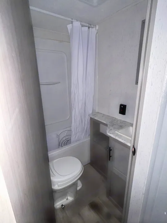 Inside a compact RV rental bathroom, featuring a toilet, shower/tub combo, and vanity with sink.. Coleman Lantern lt 2023
