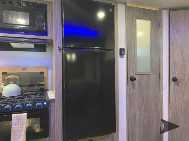 RV rental kitchen: Compact space with microwave, stovetop, oven, fridge, and a door to another section.. Forest River Cherokee Alpha Wolf 2022