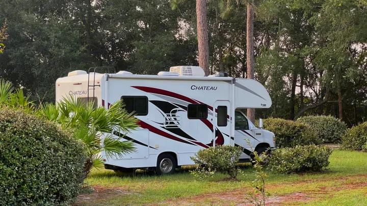 White Chateau RV rental parked at a serene, green campsite. Ideal for camping and outdoor adventures among the trees.. Thor Chateau 2022
