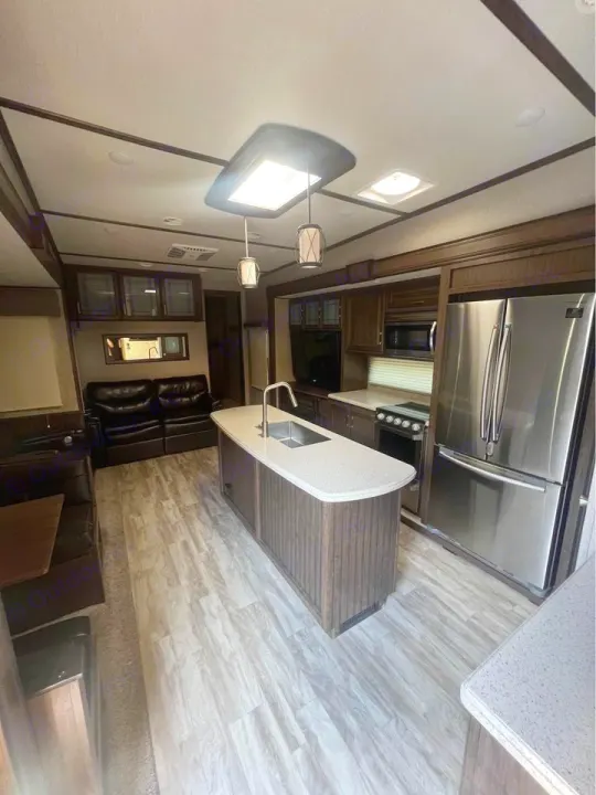 Spacious RV rental interior with a modern kitchen island, stainless appliances, and comfortable living area, all on light wood-look floors.. Grand Design Solitude 2020