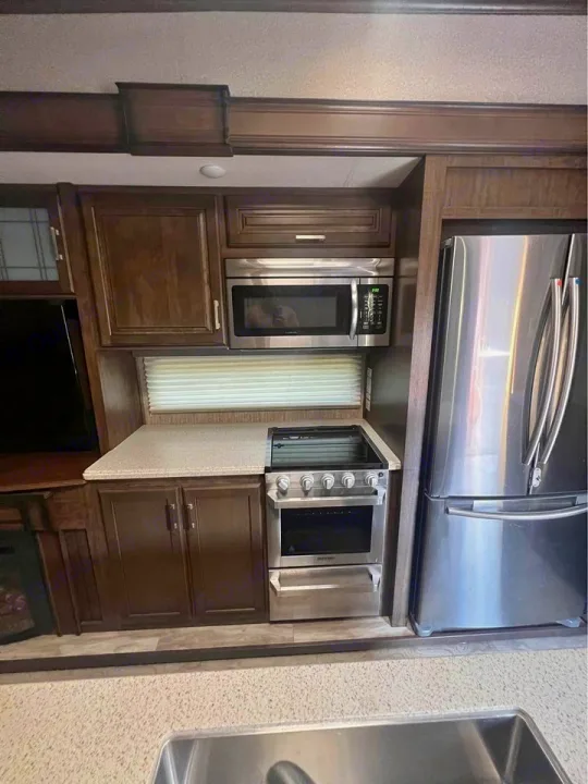 Well-appointed RV kitchen featuring stainless steel microwave, stove, and fridge. Essential amenities for your next rv rental trip.. Grand Design Solitude 2020