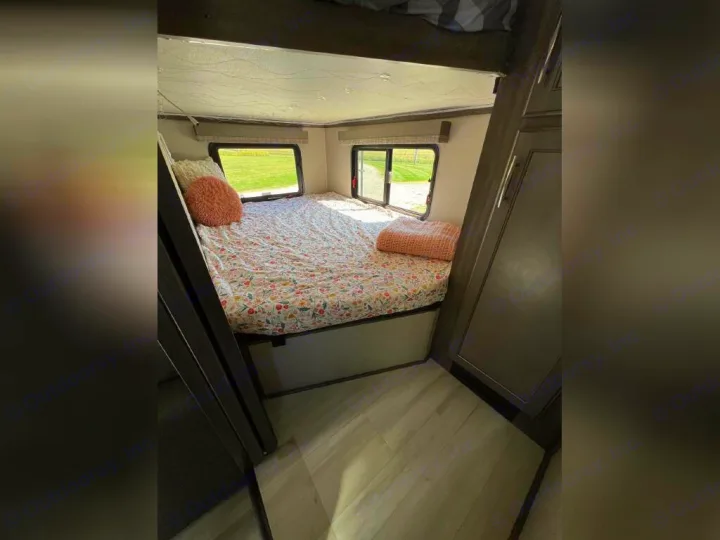 This RV rental bedroom features a comfy bed with floral bedding, a bunk above, and bright windows. Storage closet on right.. Grand Design Solitude 2020