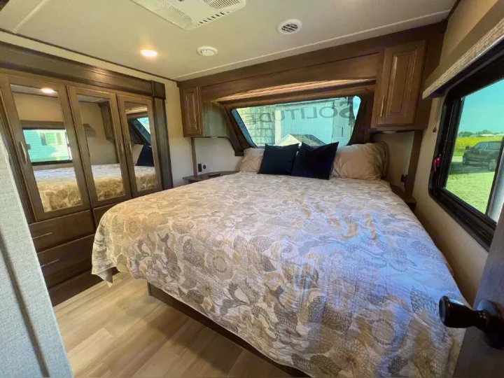 Spacious RV rental bedroom with a large bed, mirrored closet, overhead storage, and bright windows.. Grand Design Solitude 2020