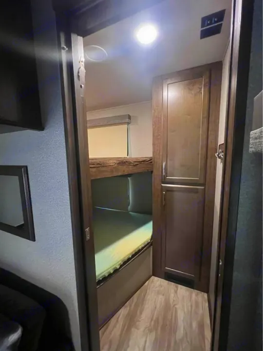 This RV rental's bright interior features cozy bunk beds and ample storage, creating a functional sleeping space.. Grand Design Solitude 2020
