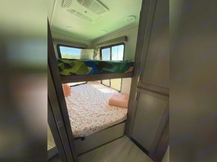 Cozy RV rental interior showcasing bright bunk beds with patterned bedding, large windows, and overhead AC unit.. Grand Design Solitude 2020
