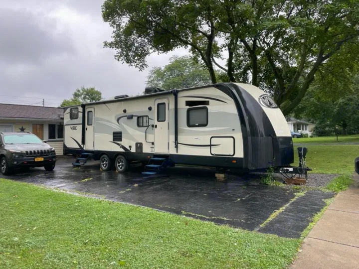 A large cream and black RV rental, possibly a travel trailer, parked on a wet driveway next to a Jeep. Ready for adventure.. Forest River Vibe 2017