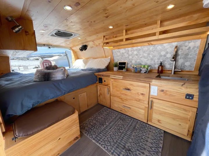 Stylish RV rental interior: bed, cozy kitchen with hexagonal tile, warm wood details, and a view of snowy hills.. Ford Ford E350 2011