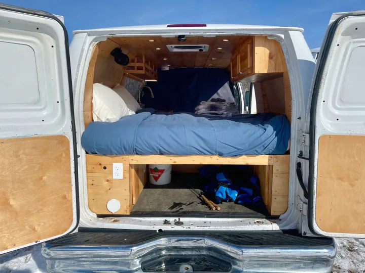 RV rental: The cozy wood-paneled interior of a white camper van with a bed, storage, and lights, viewed from the open rear doors.. Ford Ford E350 2011