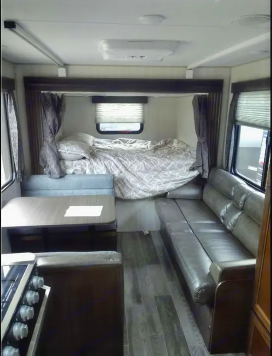 RV rental interior. A cozy, compact space with a raised bed, a dinette table, and a long gray sofa.. Forest River Cherokee Grey Wolf 2019