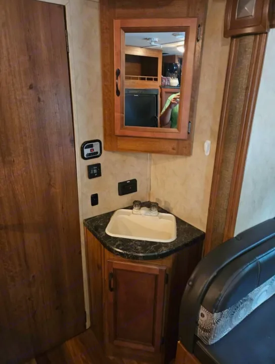 RV rental interior: compact corner sink, mirror reflecting fridge & person, wall controls, and wooden door.. Gulf Stream Ameri-Lite 2016