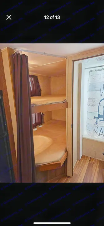 Inside an RV rental: view of two cozy bunk beds with curtains & an adjacent small bathroom with shower. Wood-look flooring.. Gulf Stream Ameri-Lite 2016