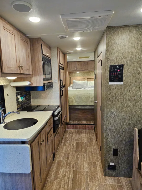 Clean, functional RV rental interior showing a modern kitchen with sink and stove, leading back to a cozy bedroom.. Forest River Sunseeker 2019