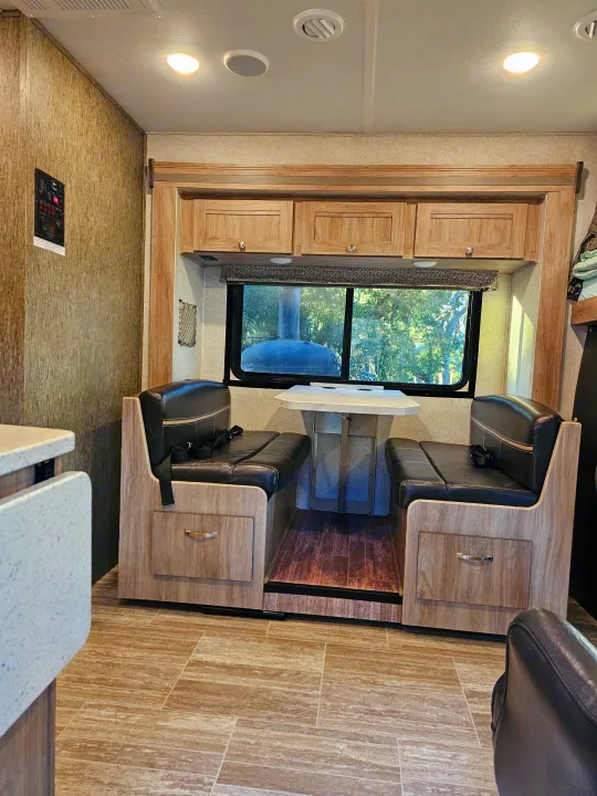 Comfortable RV rental dinette: black benches, table, wood cabinets, and large window view for travel.. Forest River Sunseeker 2019