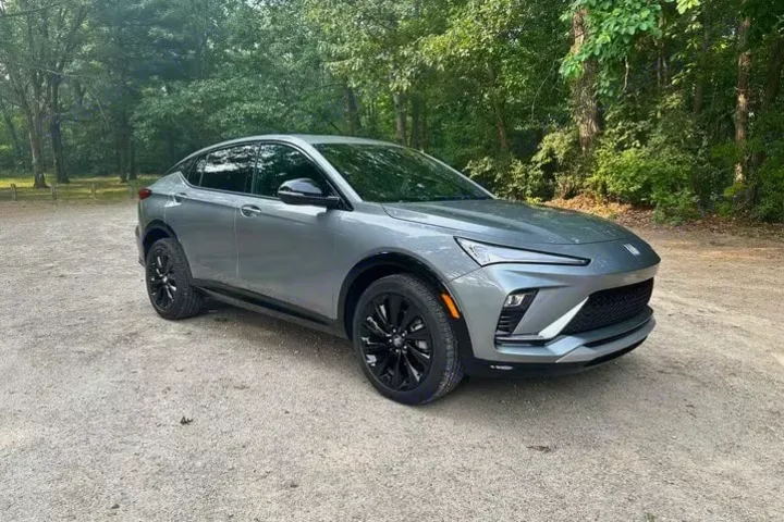 Sleek gray compact crossover on a gravel path amidst green trees. A travel option distinct from an RV rental.. Buick Envista 2024