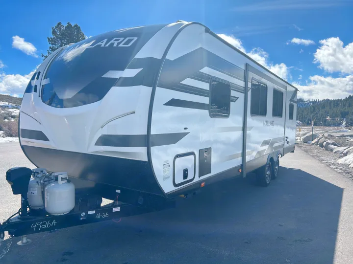 A sleek white and black Mallard **RV rental** is parked on asphalt, ready for adventure in a snowy, treed landscape.. Heartland RVs Mallard 2021