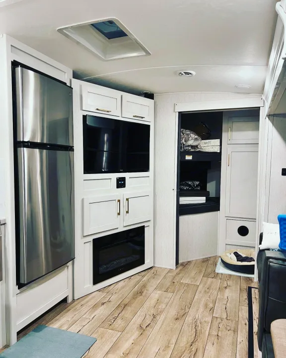 Compact RV rental interior featuring a modern fridge, TV, fireplace, storage, and cozy pet area.. Keystone RV Astoria 2903BH 2022