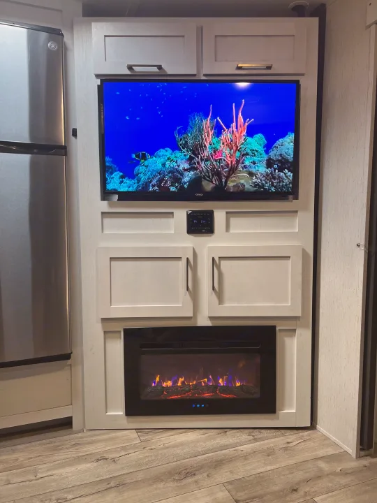 Modern RV rental interior featuring a flat-screen TV, electric fireplace, and sleek stainless steel refrigerator.. Keystone RV Astoria 2903BH 2022