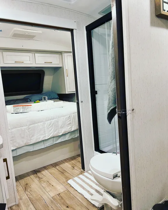 RV rental interior featuring a cozy bedroom with bed and cabinets, plus an adjacent bathroom with shower and toilet.. Keystone RV Astoria 2903BH 2022