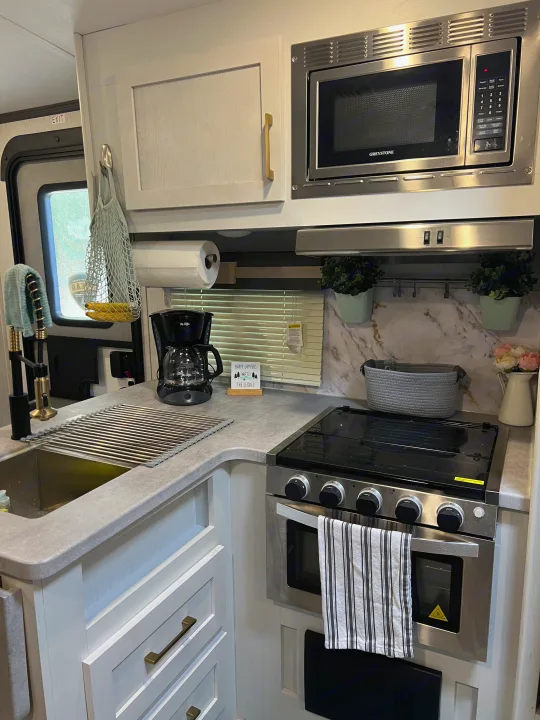 Modern RV rental kitchen featuring a microwave, stove, sink, and coffee maker, offering a bright, functional space.. Keystone RV Astoria 2903BH 2022
