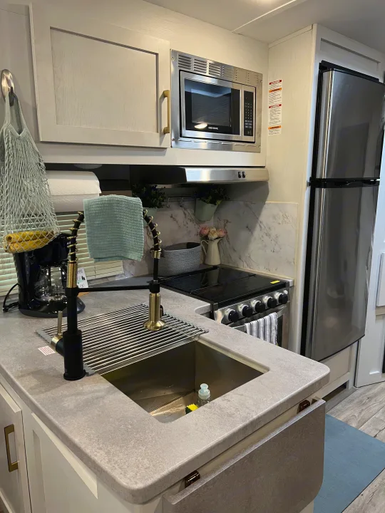 Modern RV rental kitchen with sleek grey counters, stainless appliances, and stylish gold fixtures.. Keystone RV Astoria 2903BH 2022